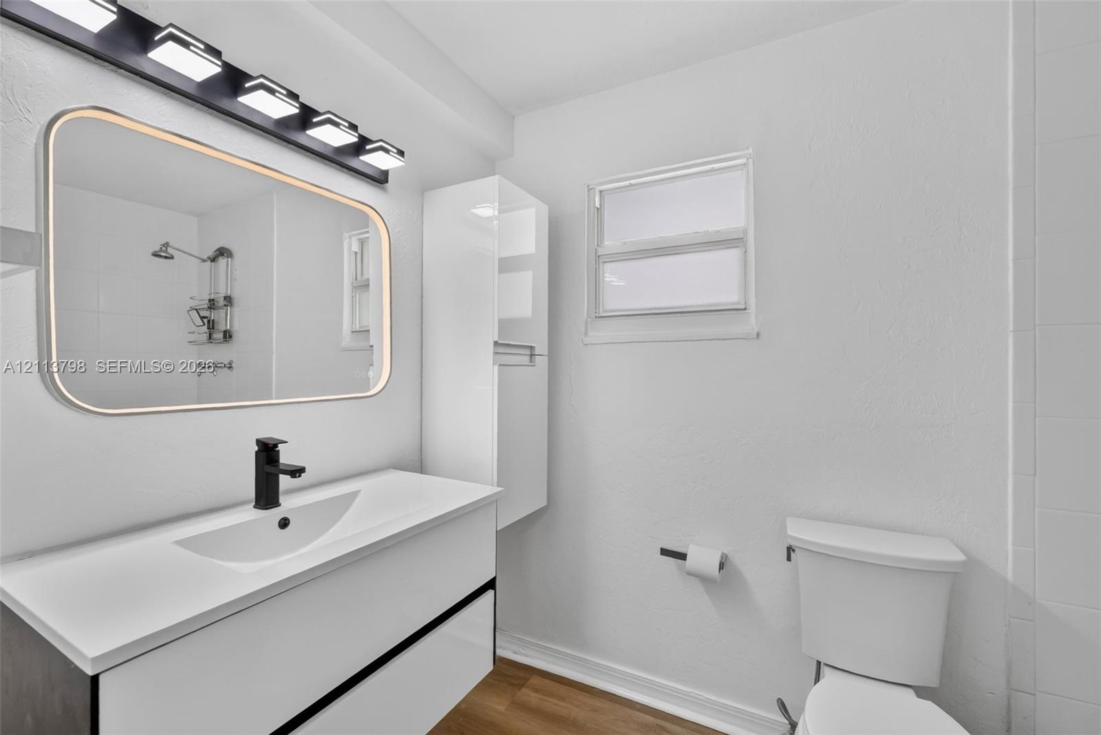 Bathroom featuring a floating vanity with a integrated basin, matte black faucet, wall-mounted storage cabinet, and large rectangular mirror with peri