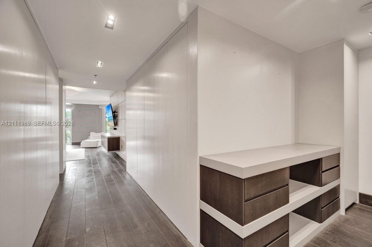 Hallway featuring wood-finish flooring, extensive floor-to-ceiling built-in cabinetry with a seamless finish, recessed ceiling lighting, and a custom 