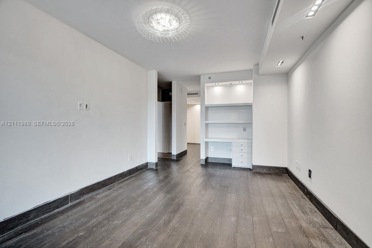 Wood-finish flooring, built-in shelving with integrated lighting, custom desk cabinetry with drawer storage, circular decorative ceiling fixture, and 