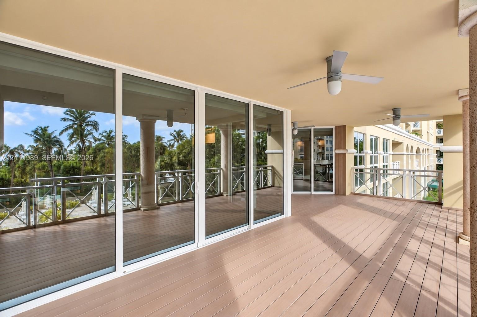 Covered outdoor balcony featuring wood-finish flooring, full-height sliding glass doors, decorative support columns, and ceiling-mounted fans