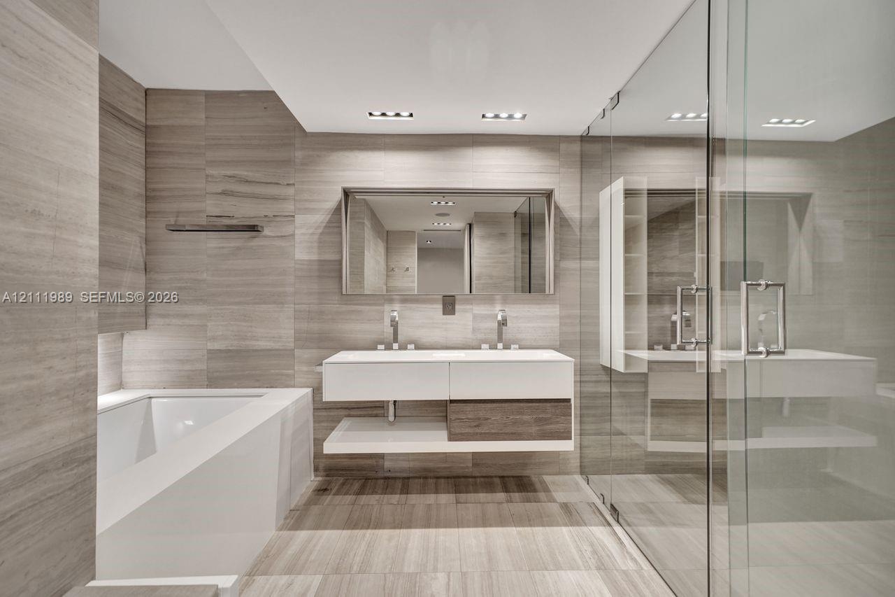 Floating dual vanity with integrated countertop, wall-to-wall linear tile surfacing, recessed ceiling lighting, glass-enclosed shower, and deep-profil