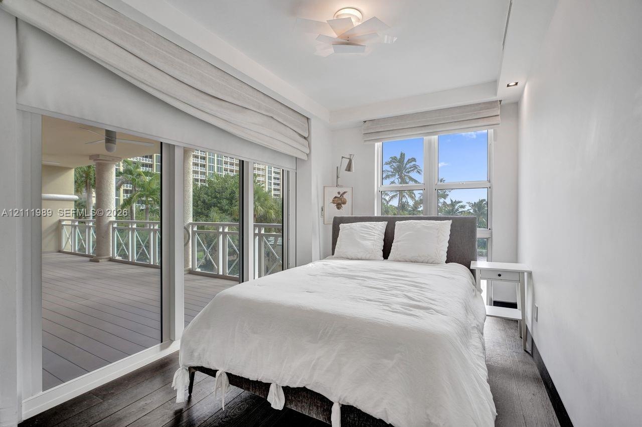 Sliding glass doors opening to a covered balcony, wood-finish flooring, recessed ceiling lighting, and custom window treatments