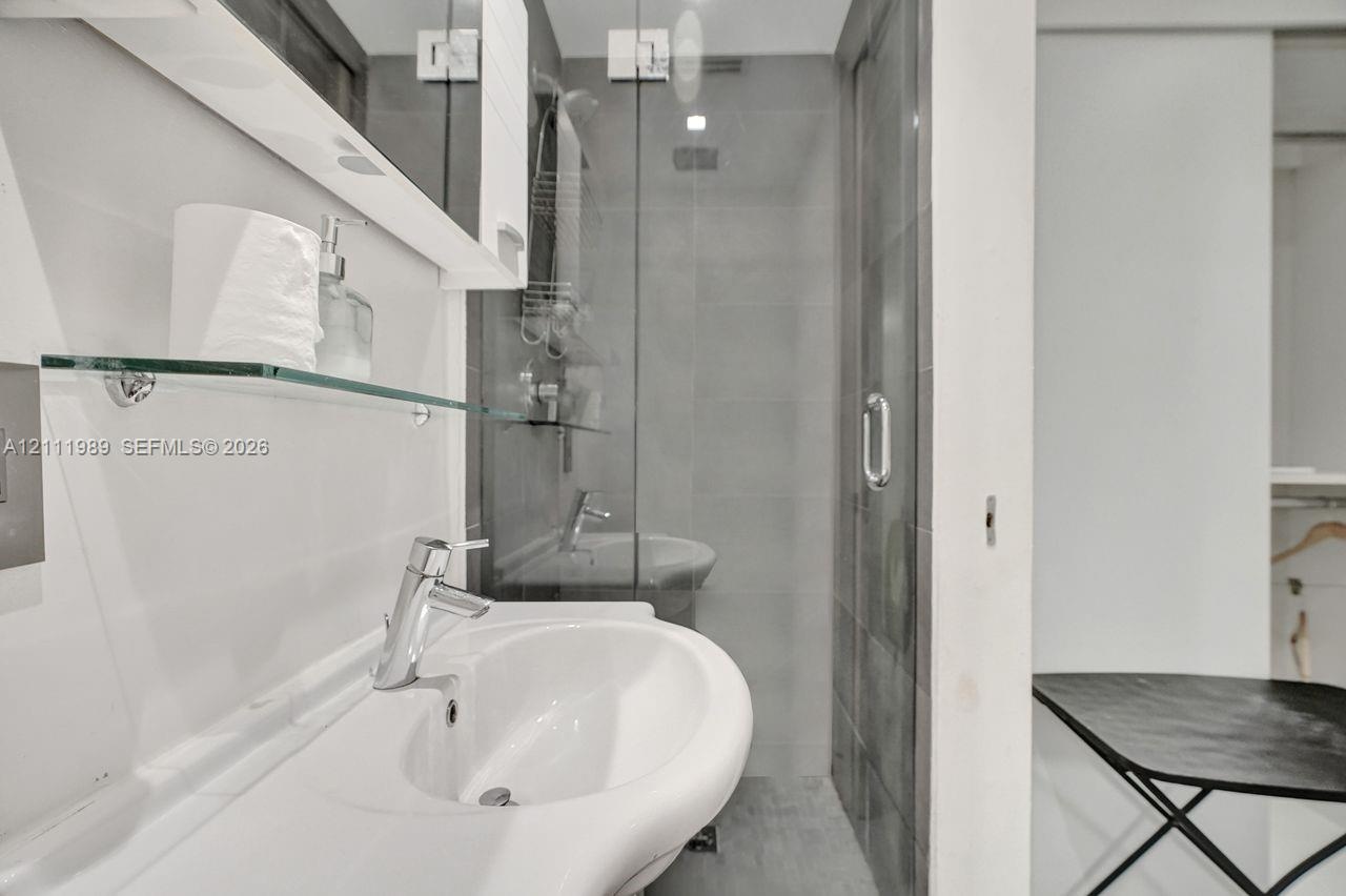 Bathroom featuring a wall-mounted vanity, stainless steel single-handle faucet, glass-enclosed shower with full-height tile, and integrated mirrored m