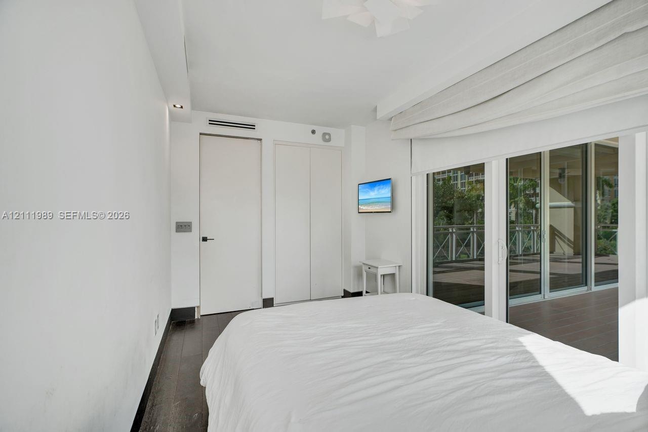 Room featuring dark wood-finish flooring, floor-to-ceiling sliding glass doors, built-in closet cabinetry, and minimalist white window treatments