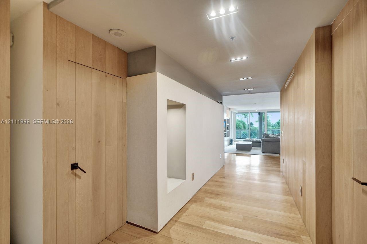 Interior hall featuring natural wood-finish paneling, wood-finish flooring, recessed lighting, and a built-in display niche with matte black hardware