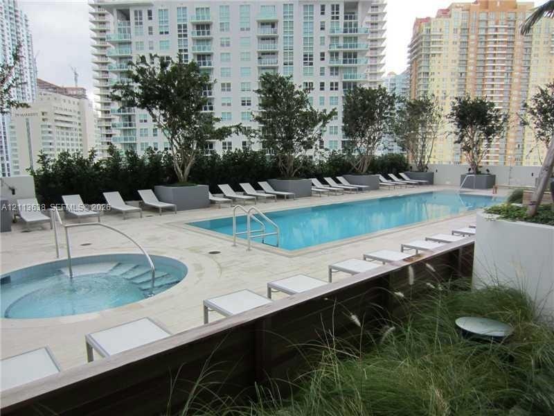Rooftop terrace featuring an in-ground swimming pool, separate circular spa, stone-finish decking, and built-in landscape planters with mature trees