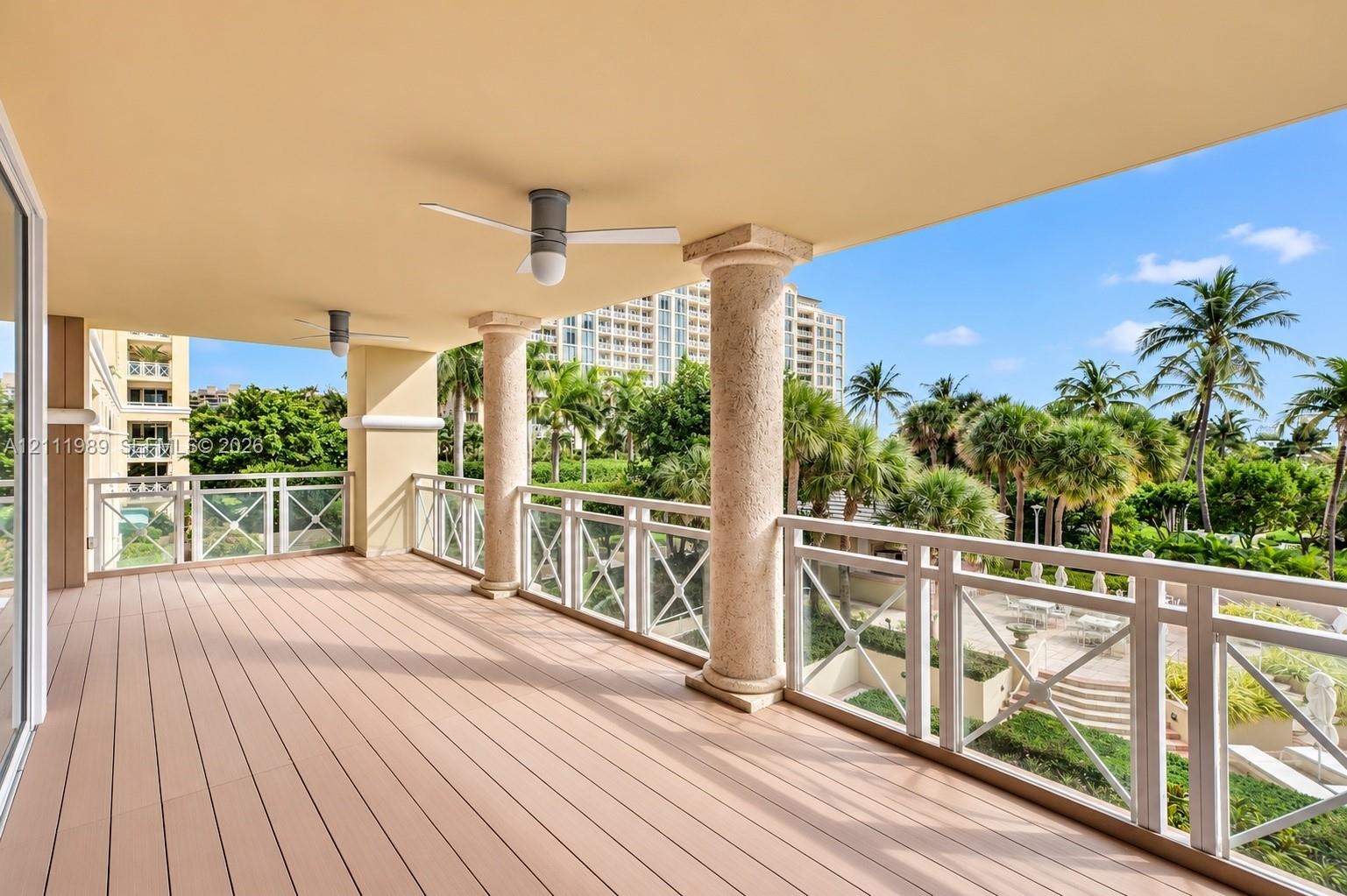 Covered balcony featuring wood-finish flooring, structural stone-finish columns, white cross-patterned railings, and ceiling-mounted fans