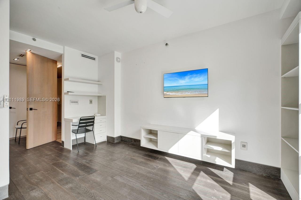 Wood-finish flooring, built-in white desk with overhead shelving, wall-mounted cabinetry, integrated floor-to-ceiling shelving unit, and solid-core li