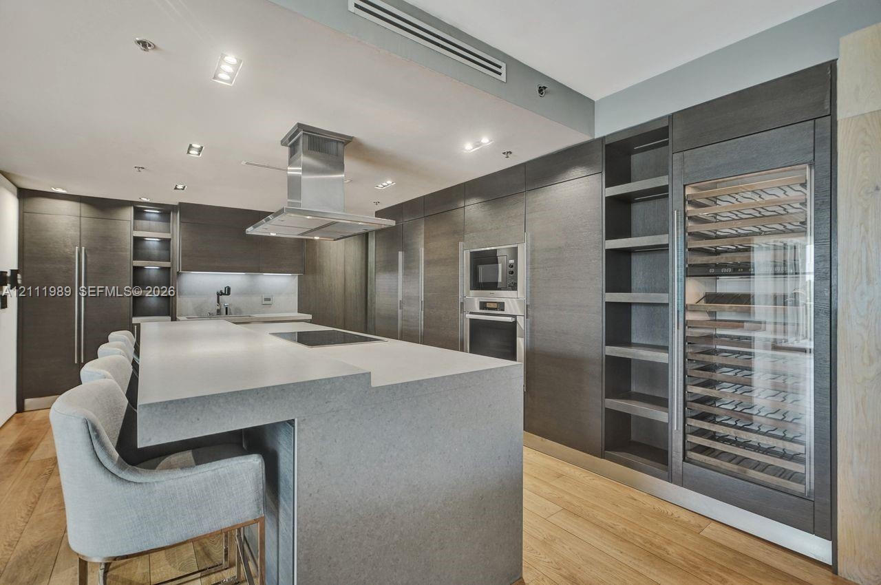 Kitchen featuring wood-finish flooring, a large island with a stone-surfaced countertop, integrated stainless steel appliances, dark wood-tone cabinet