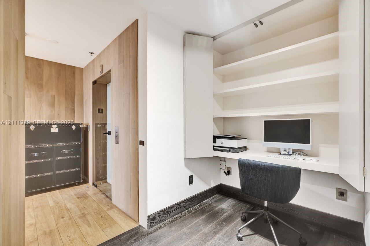 Built-in wall desk with overhead shelving, wood-finish flooring, wood wall paneling, and a dedicated alcove entry