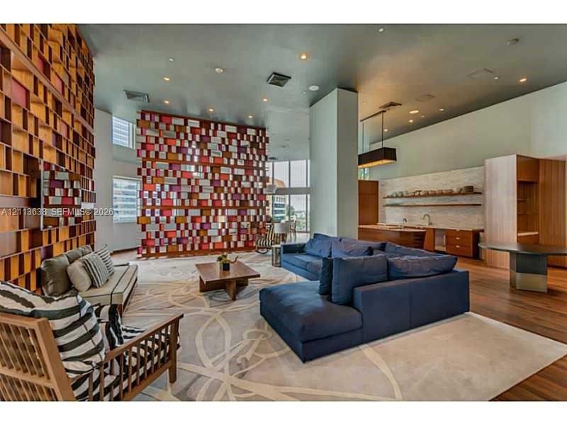 Open-concept living space featuring high ceilings, a prominent floor-to-ceiling geometric wood-toned feature wall, wood-finish flooring, and a built-i