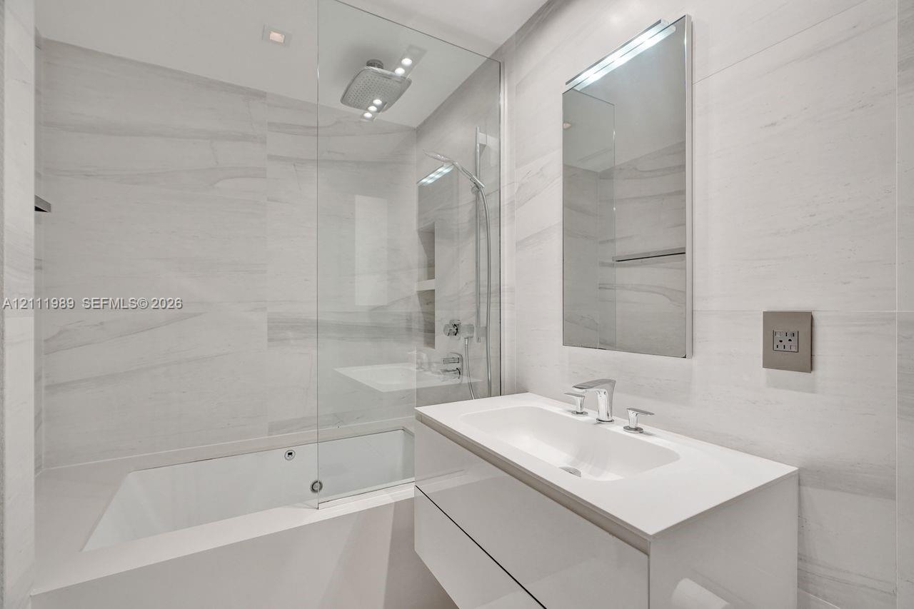 Bathroom featuring full-height wall tiling, a floating white vanity with an integrated basin, a frameless glass shower enclosure, a ceiling-mounted ra