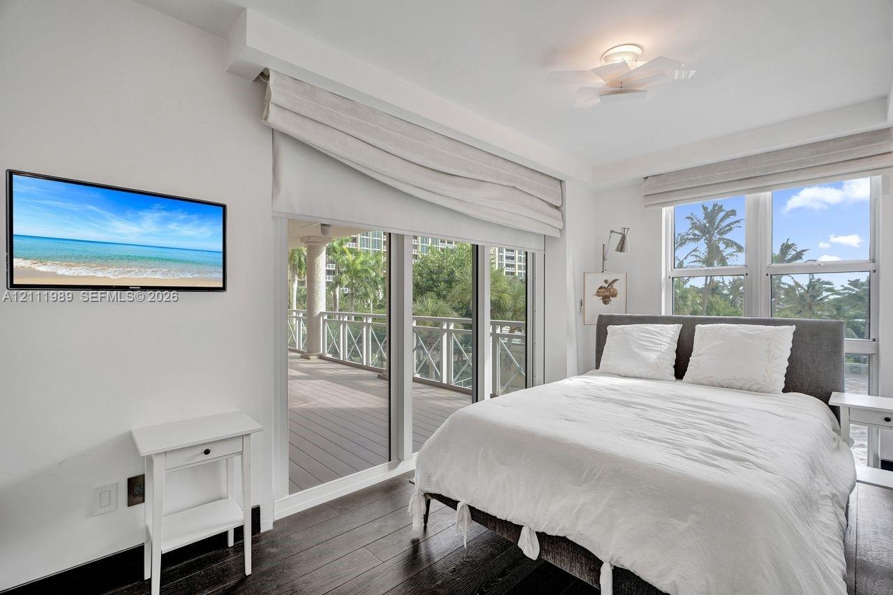 Dark wood-finish flooring, floor-to-ceiling glass sliding doors, private balcony with decorative railing, and ceiling-mounted light fixture with integ
