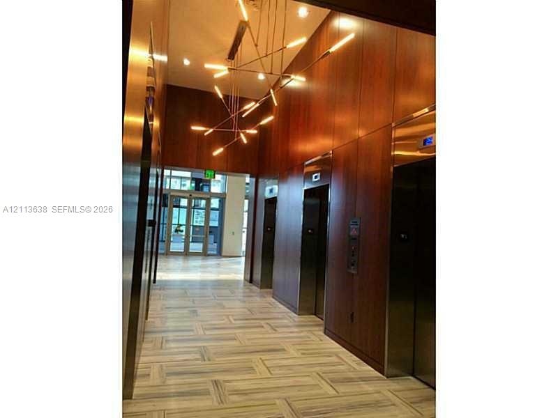 Lobby featuring floor-to-ceiling wood-paneled walls, neutral stone flooring in a herringbone pattern, modern multi-arm pendant lighting, and polished 