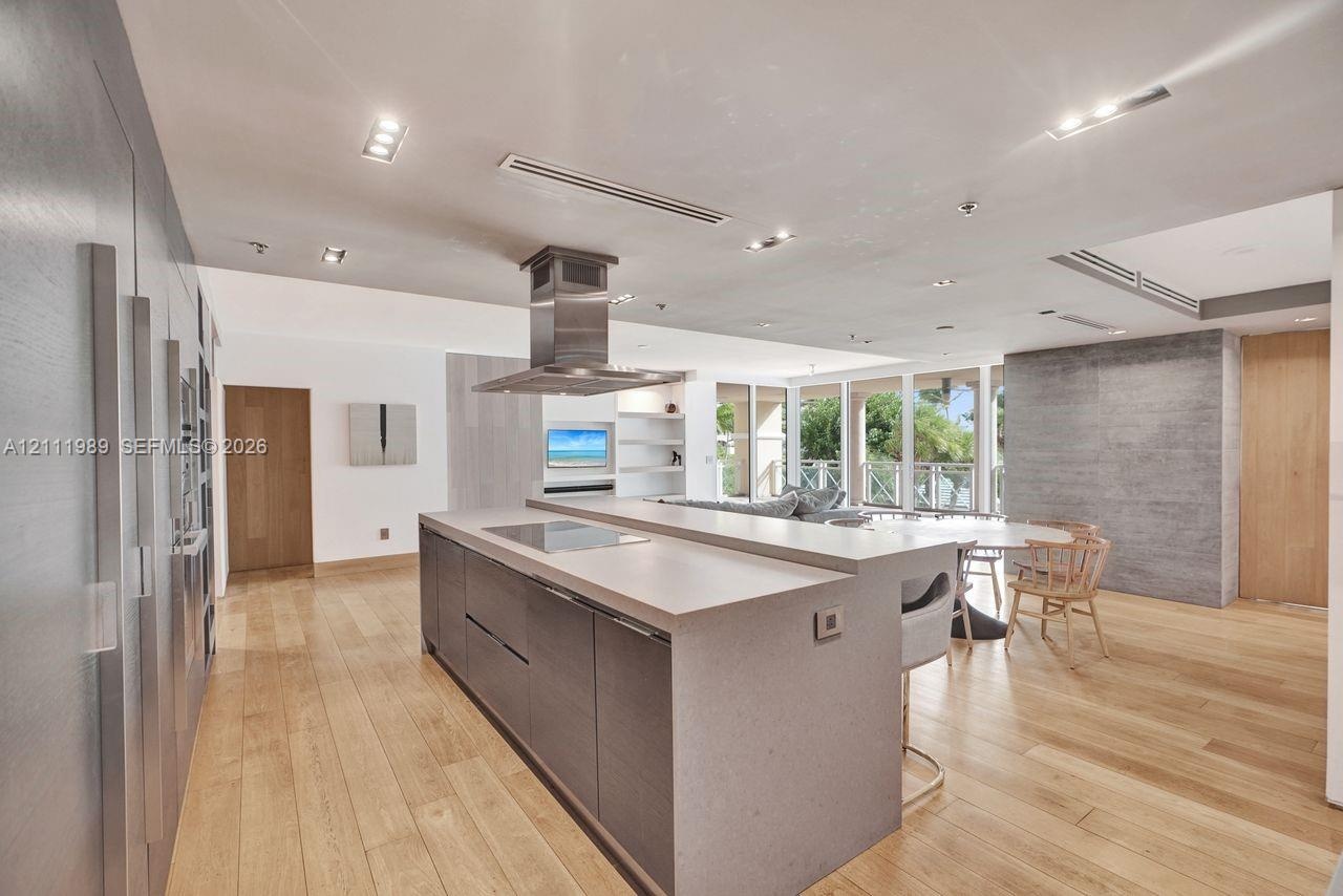 Chef’s kitchen featuring an expansive center island with stone countertop, stainless steel range hood, built-in cabinetry with integrated appliances, 