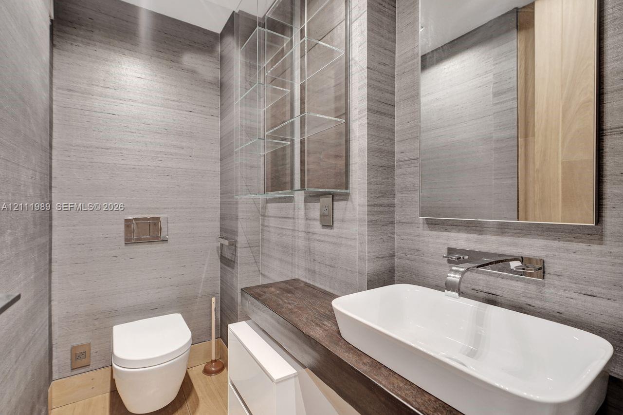 Wall-to-wall stone-finish paneling, wall-mounted toilet with chrome actuator, custom vanity with wood-finish countertop, rectangular vessel sink, and 