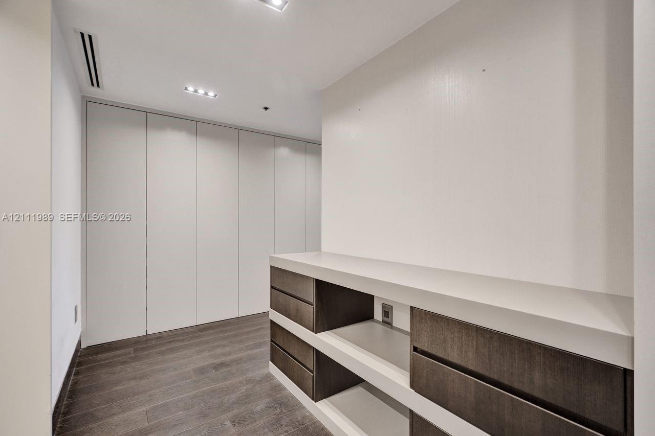 Built-in floor-to-ceiling cabinetry with white paneling, wood-finish flooring, custom low-profile shelving with dark-toned drawers, and recessed ceili