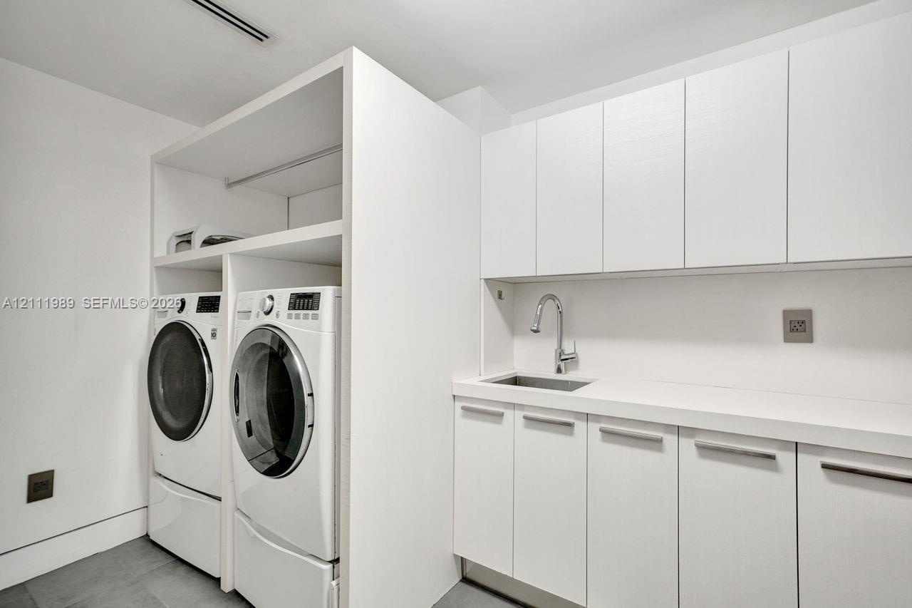 Laundry area featuring white flat-panel cabinetry, a quartz countertop, a stainless steel undermount sink with a gooseneck faucet, and integrated buil