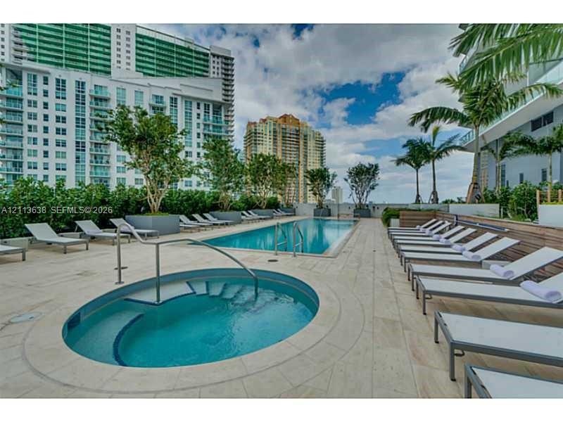 Swimming pool and circular spa with stone decking, metal handrails, and perimeter landscaping