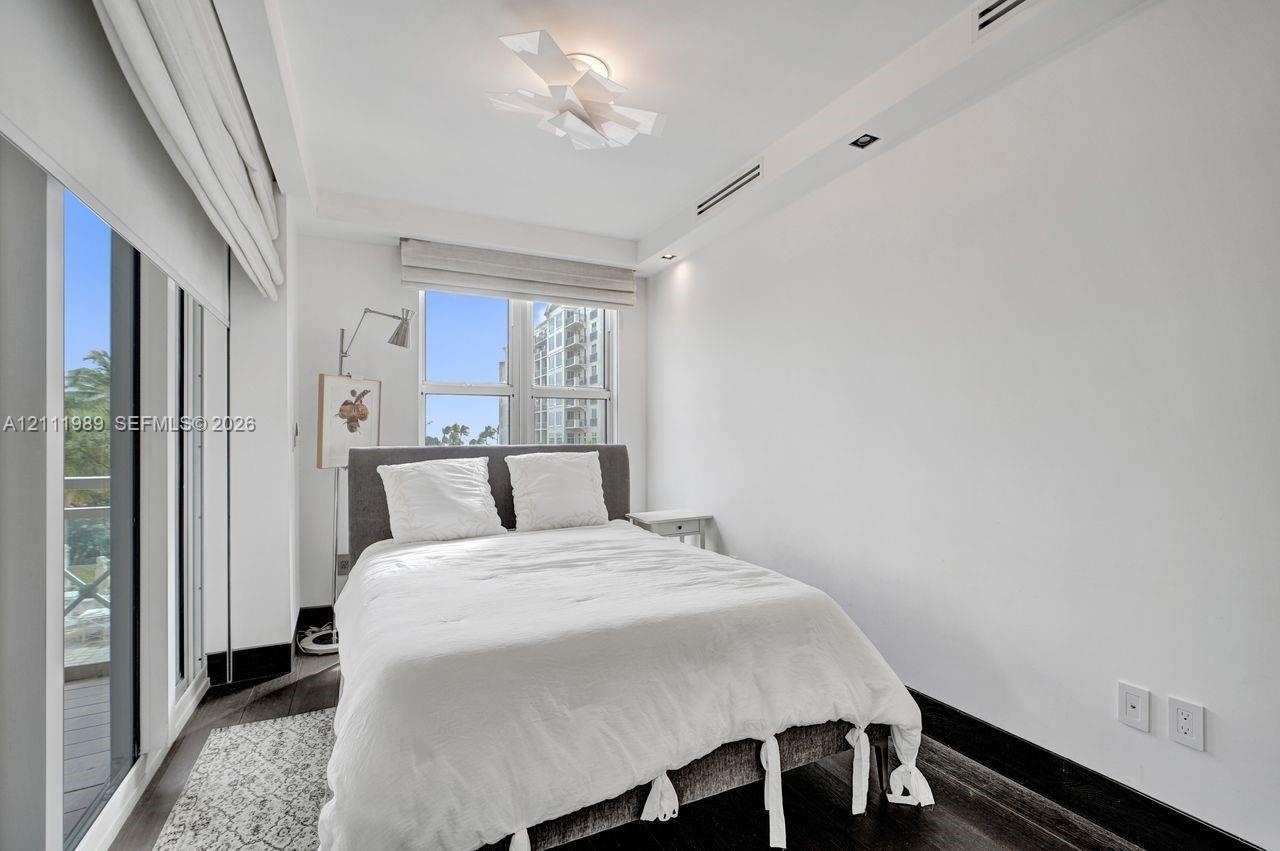 Floor-to-ceiling sliding glass doors, dark-toned wood-finish flooring, recessed lighting, sculptural ceiling fixture, and dual-window wall configurati
