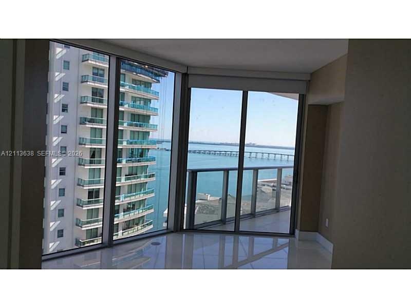 Floor-to-ceiling wrap-around windows, sliding glass door, private balcony with metal railing, and polished stone-finish flooring