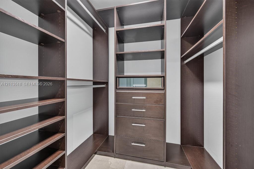 Custom walk-in storage system featuring dark wood-finish cabinetry, built-in shelving, integrated hanging rods, and a centralized unit with four drawe