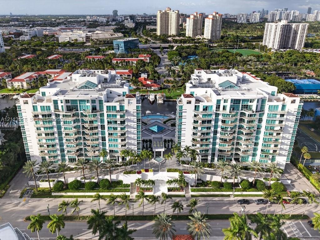 Aerial view of a multi-story residential complex featuring private balconies, central outdoor swimming pool, paved entryway, and manicured landscaping