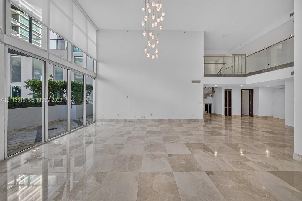 Expansive interior space featuring double-height ceilings, floor-to-ceiling windows, polished stone flooring, a multi-pendant light fixture, and a mez