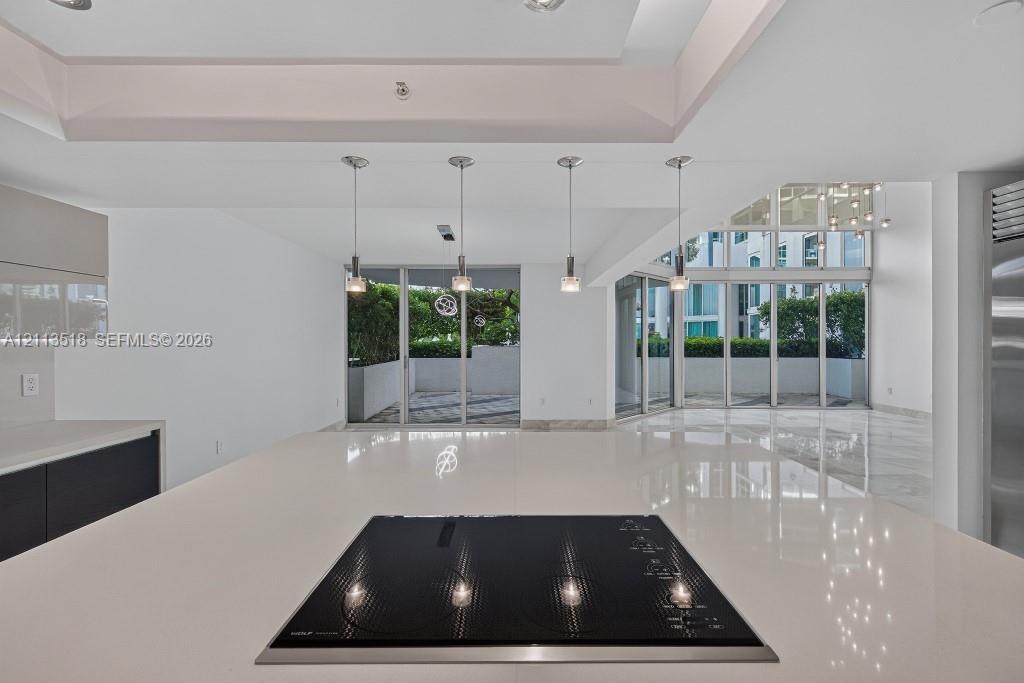 Kitchen island featuring a solid surface countertop, built-in induction cooktop, four pendant light fixtures, and multi-panel floor-to-ceiling glass s