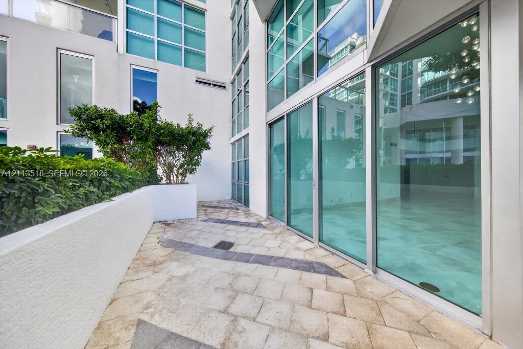 Private terrace featuring large-format stone pavers, integrated concrete planter beds with mature shrubbery, and floor-to-ceiling glass wall panels wi