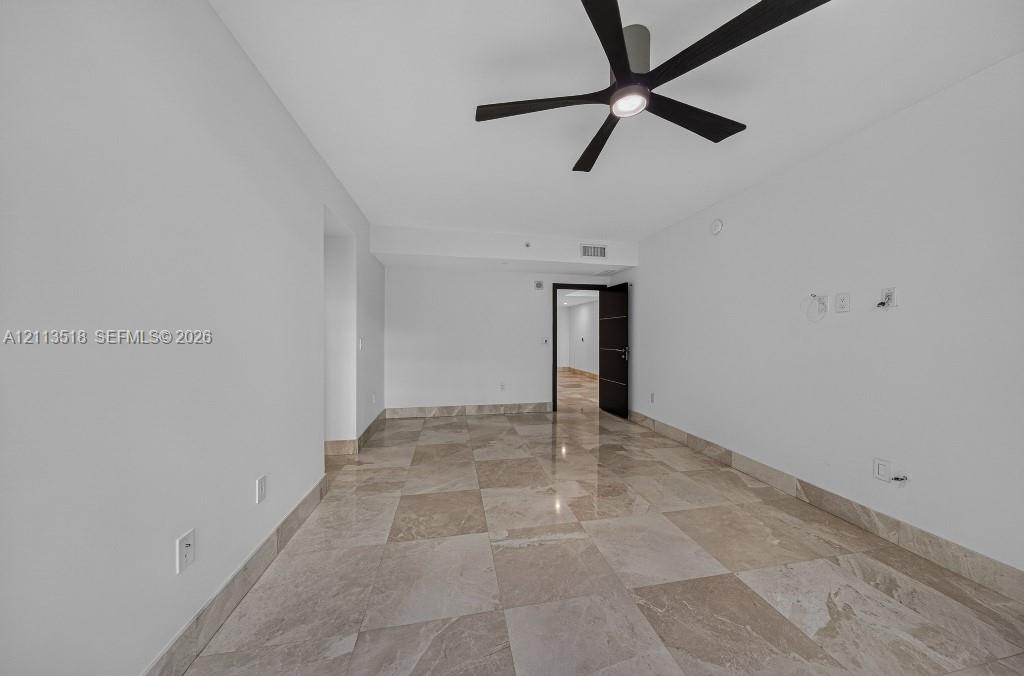 Spacious room featuring polished large-format stone tile flooring, neutral wall finishes, and a contemporary matte black ceiling fan with integrated l