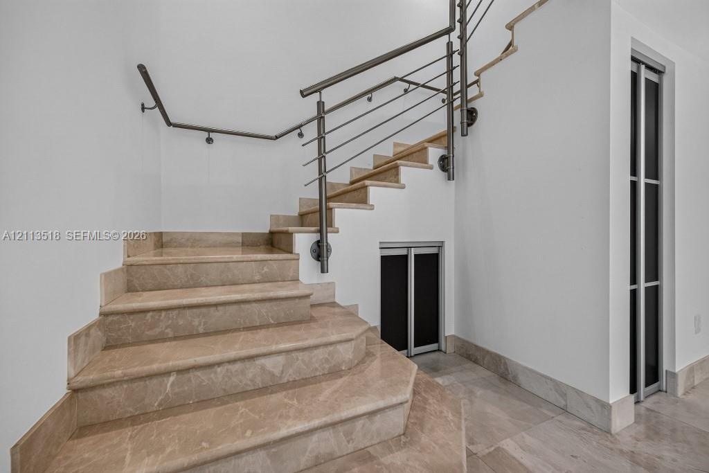 Staircase featuring stone treads, metal industrial-style railing, and built-in storage access