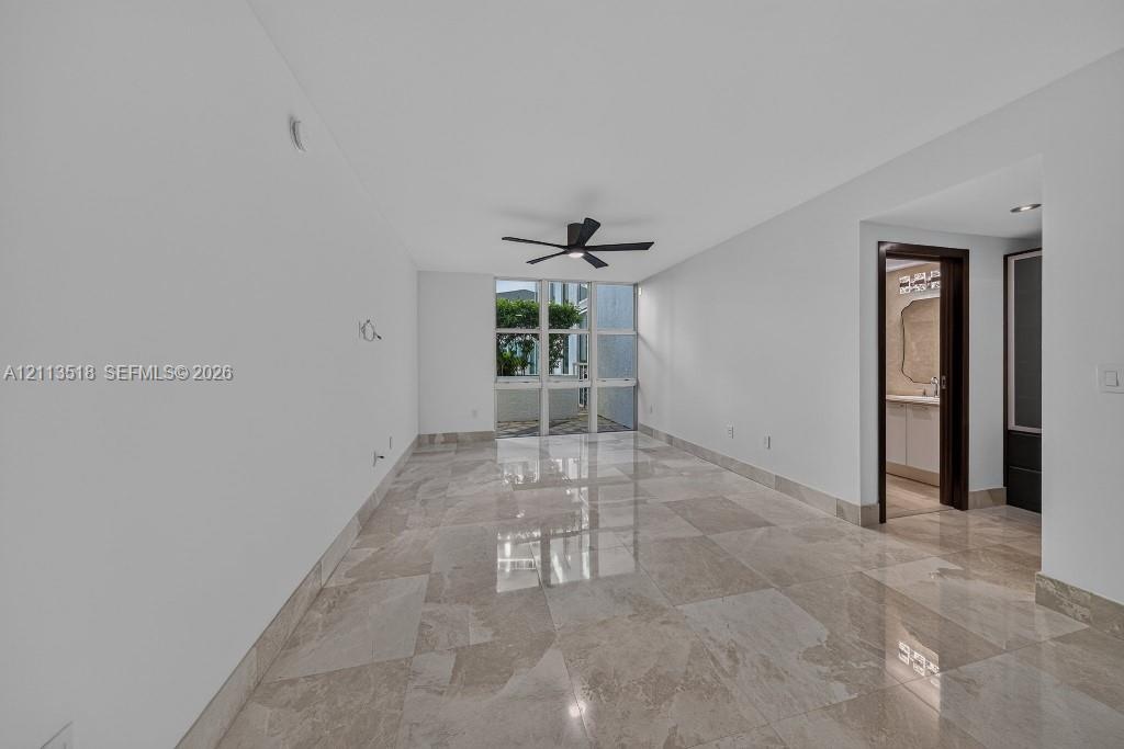 Interior space featuring polished natural stone flooring, floor-to-ceiling windows, and a matte black ceiling fan