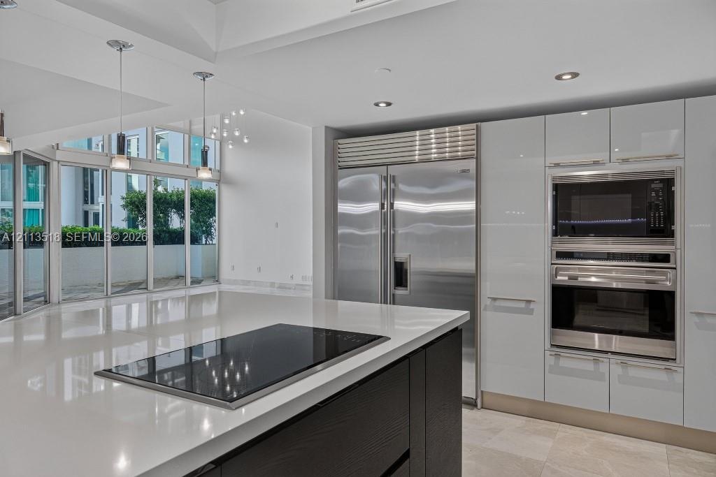 Kitchen featuring high-gloss cabinetry, a large central island with an integrated cooktop, stainless steel professional-grade appliances, recessed lig