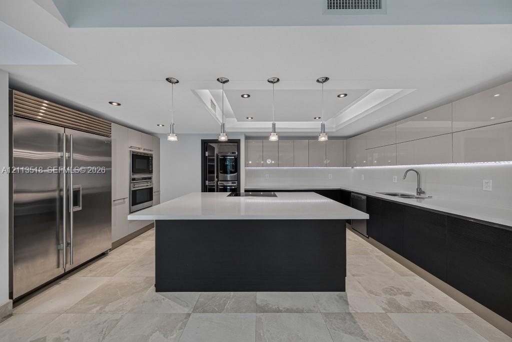 Modern kitchen featuring a central island with a stone countertop, high-gloss cabinetry, stainless steel refrigerator, recessed ceiling lighting, and 