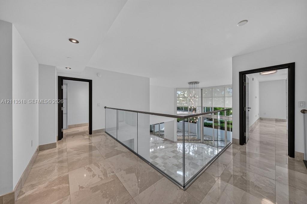 Polished tile flooring, glass panel railing with a metal handrail, recessed lighting, and dark-toned door frames