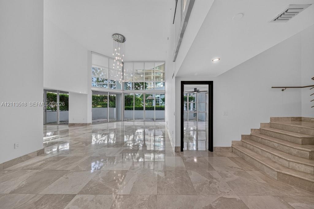 Double-height ceilings, floor-to-ceiling glass wall, polished stone flooring, custom multi-light chandelier, and stone staircase