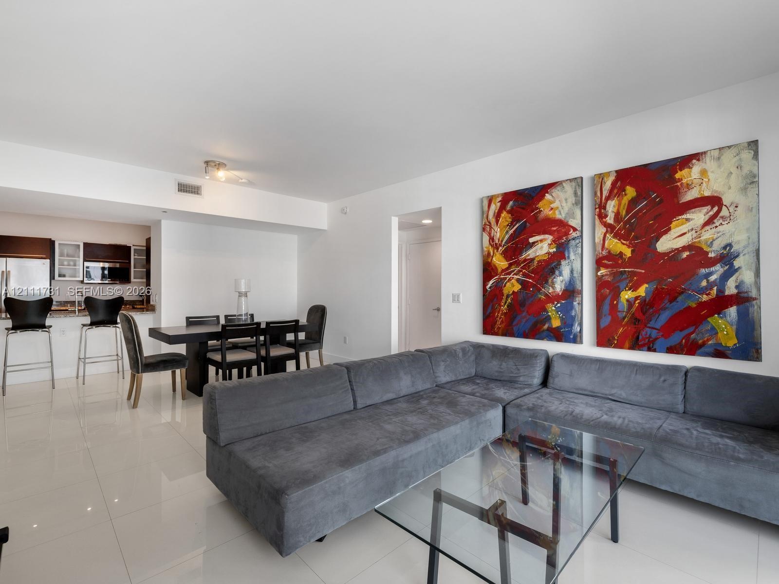 Open floor plan featuring polished tile flooring, recessed lighting, and kitchen with dark-finish cabinetry and stone-surface breakfast bar