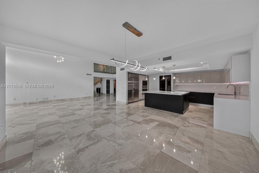 Open-concept interior featuring large-format tile flooring, a kitchen island with a neutral countertop, stainless steel built-in appliances, flat-pane