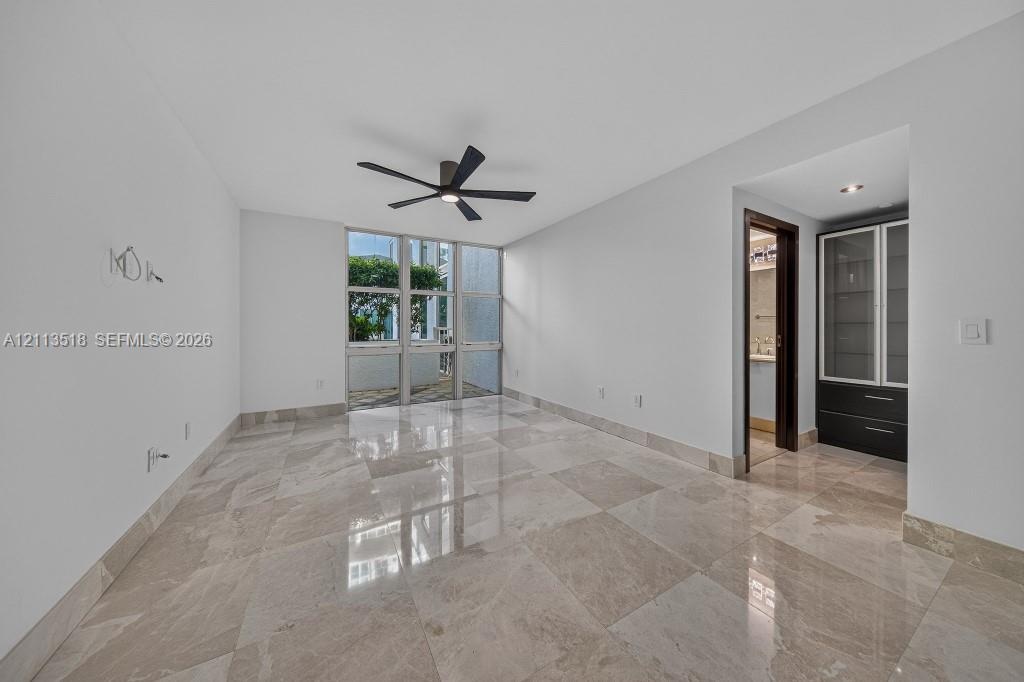 Interior space featuring large-format stone tile flooring, floor-to-ceiling windows, a ceiling fan with integrated lighting, and built-in cabinetry wi