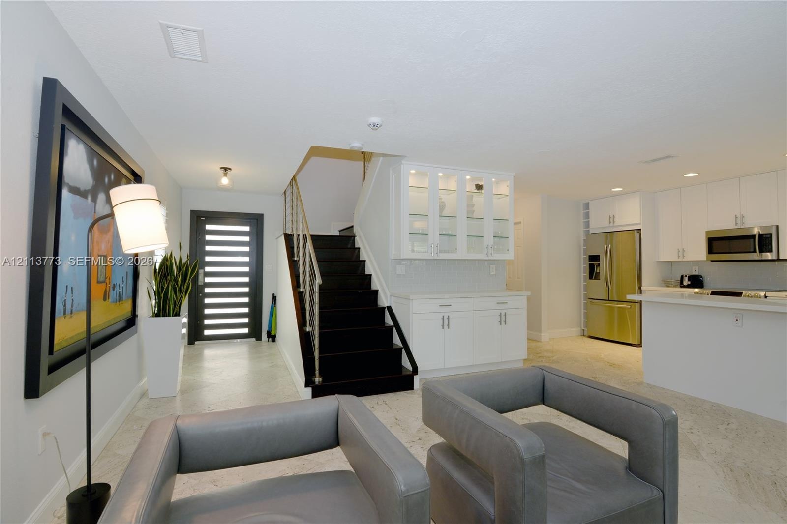 Modern entryway featuring a multi-paneled glass front door, stone-finish flooring, and a staircase with dark treads and metal railings