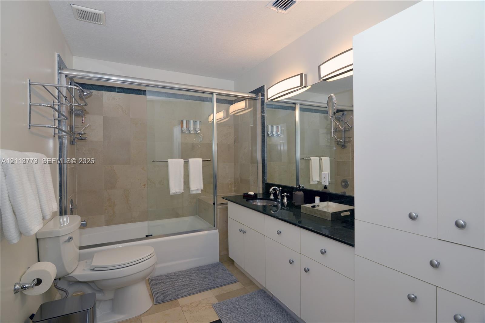 Bathroom featuring a vanity with dark stone countertop, white built-in cabinetry, dual wall-mounted vanity lights, and a tub-shower combination enclos