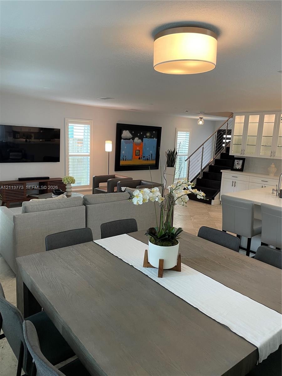 Open concept interior featuring stone tile flooring, built-in glass-front cabinetry, a contemporary drum-style ceiling light, and a staircase with met