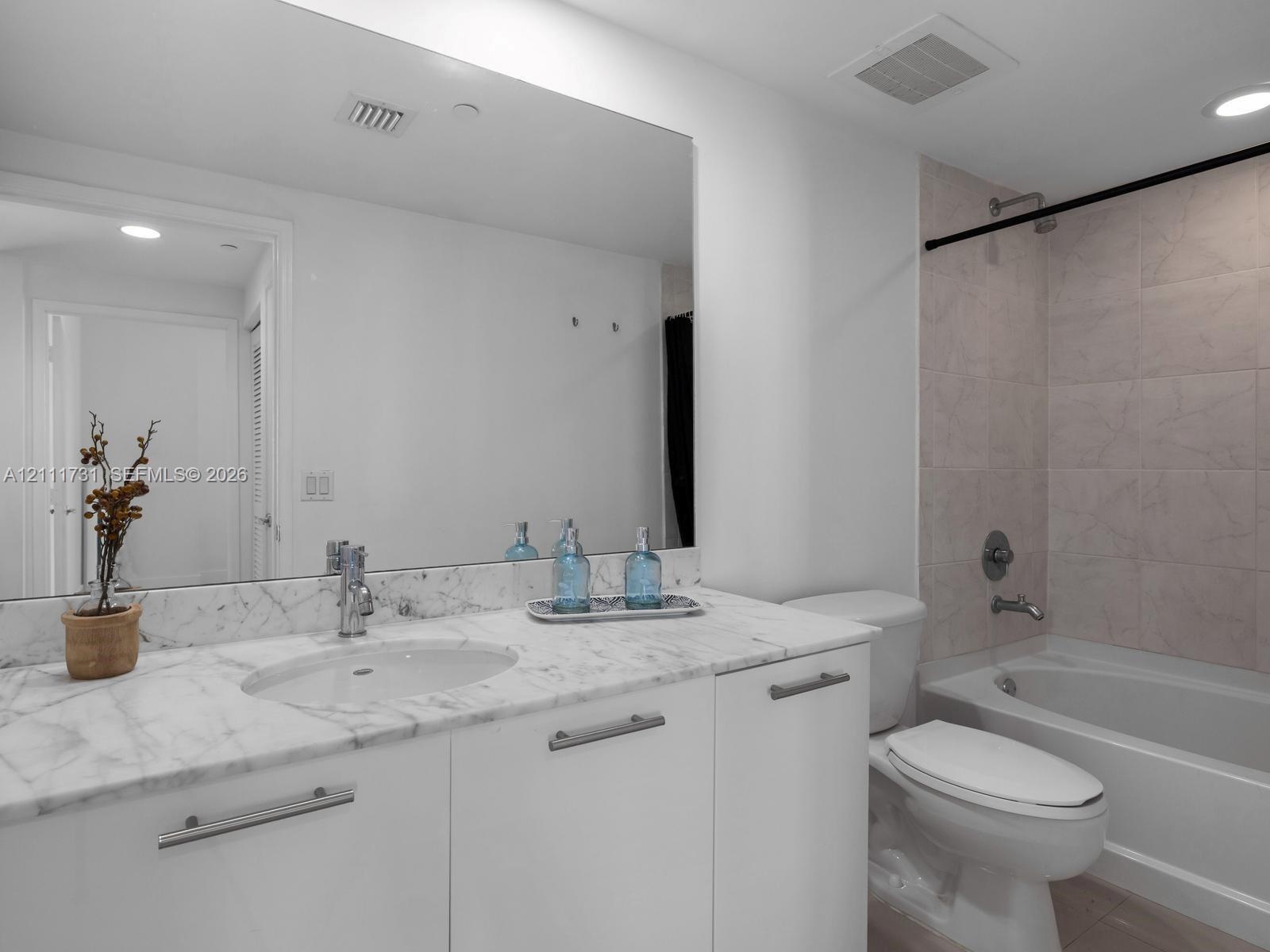 Bathroom featuring a stone-surface vanity with an integrated basin, flat-panel white cabinetry with metallic hardware, a full-width mirror, and a tile