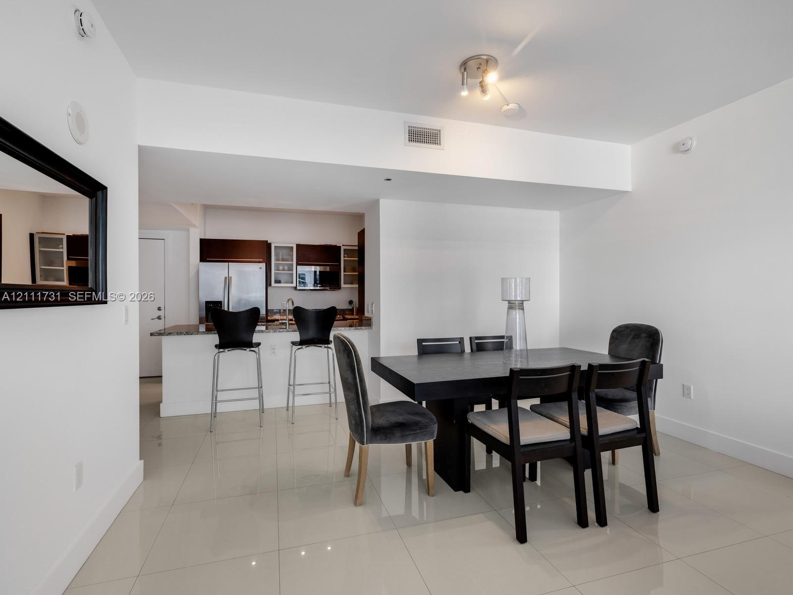 Open floor plan featuring polished tile flooring, kitchen with dark cabinetry, stone countertops, breakfast bar, and recessed track lighting