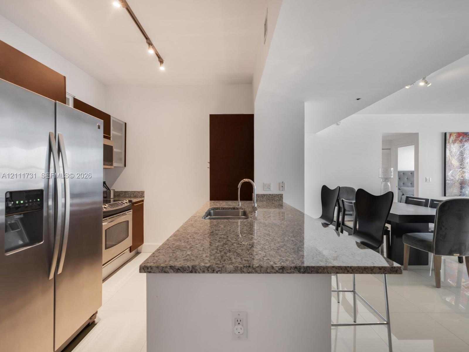 Kitchen featuring an island with stone countertop, stainless steel appliances, dark cabinetry, and track lighting