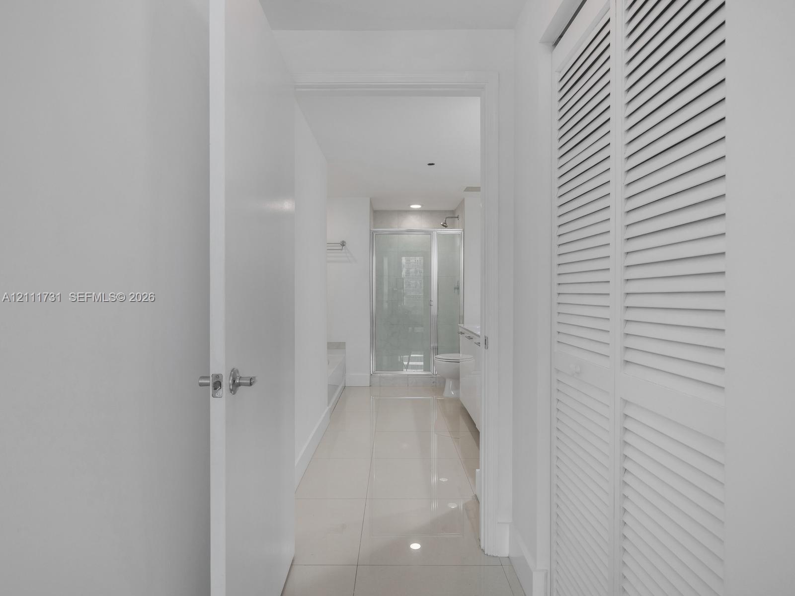 Polished large-format tile flooring, white louvered bifold doors, and a glass-enclosed shower stall