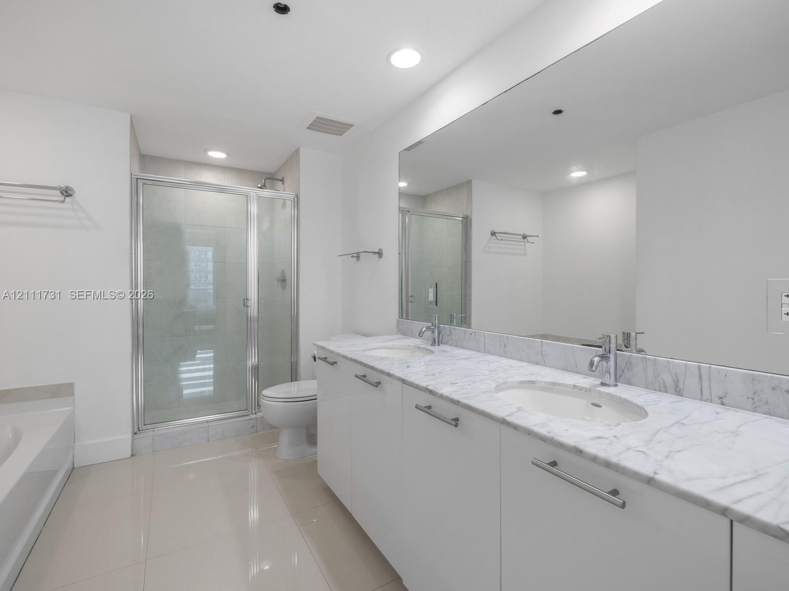 Double vanity featuring a stone-finish countertop, undermount sinks, contemporary cabinetry with metal hardware, and an expansive wall-to-wall mirror