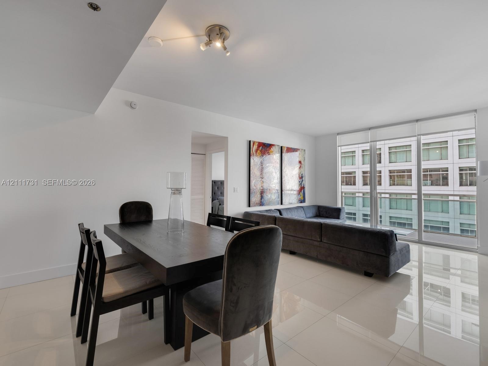 Open-concept interior featuring large-format tile flooring, recessed lighting, and floor-to-ceiling windows with sliding glass door access to a balcon