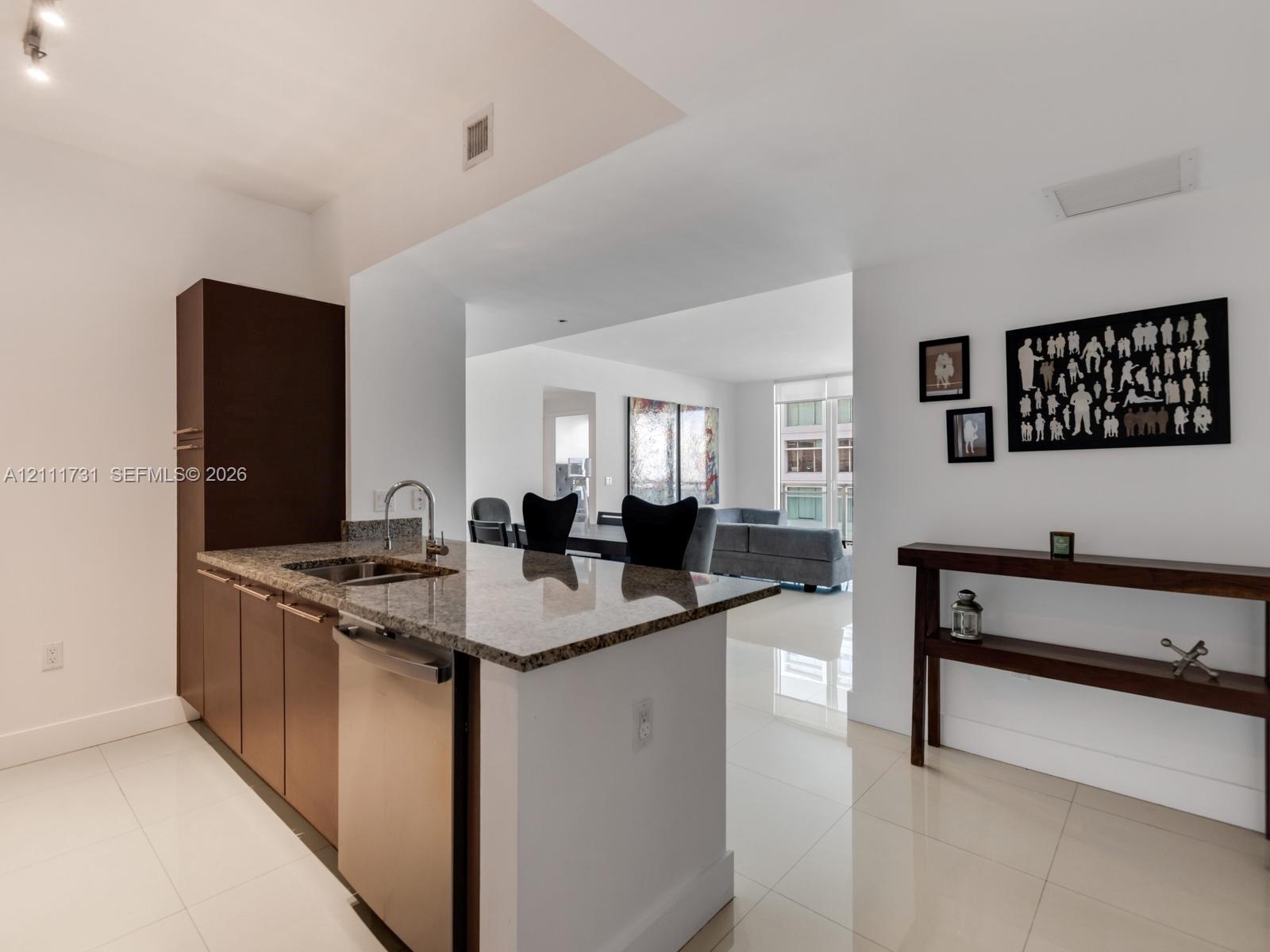 Kitchen featuring a stone-surface island, undermount sink with a gooseneck faucet, stainless steel dishwasher, full-height dark-toned cabinetry, and p